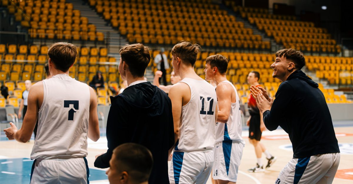 Grupa koszykarzy w białych strojach przy linii bocznej boiska, która kibicuje swojej drużynie