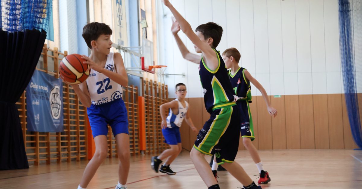 Młody zawodnik próbuje podać piłkę, a zielony go blokuje.