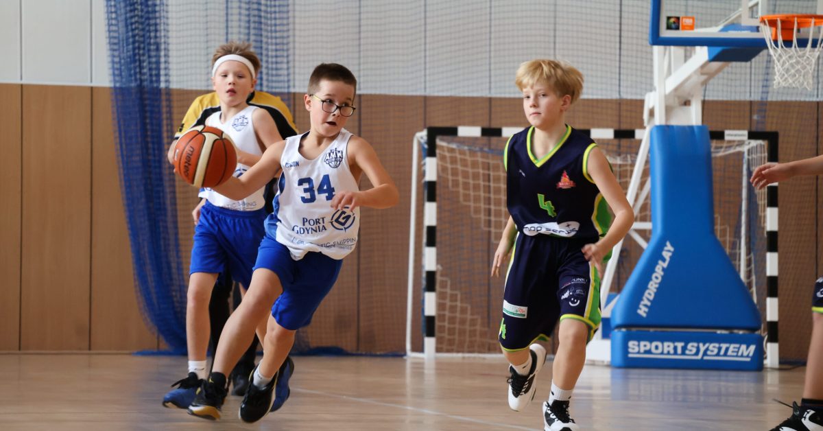 Zawodnicy w niebieskich i zielonych strojach biegną po boisku, trzymając piłkę w trakcie szybkiej akcji.