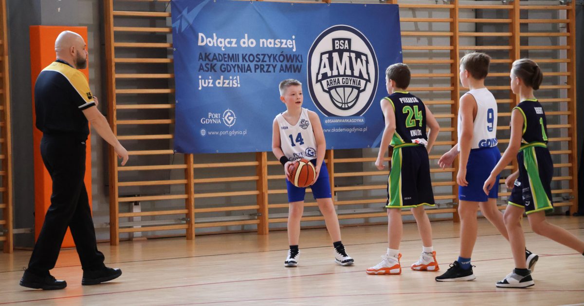 Zawodnik w białej koszulce trzyma piłkę szukając komu ją podać.