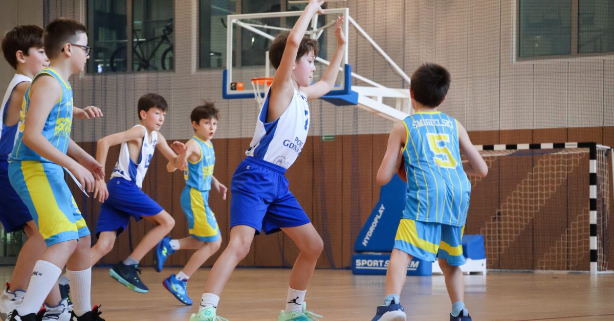 Akcja na boisku– zawodnik w niebiesko- żółtym stroju wykonuje rzut, podczas gdy przeciwnik w biało-niebieskim stroju próbuje go zablokować.