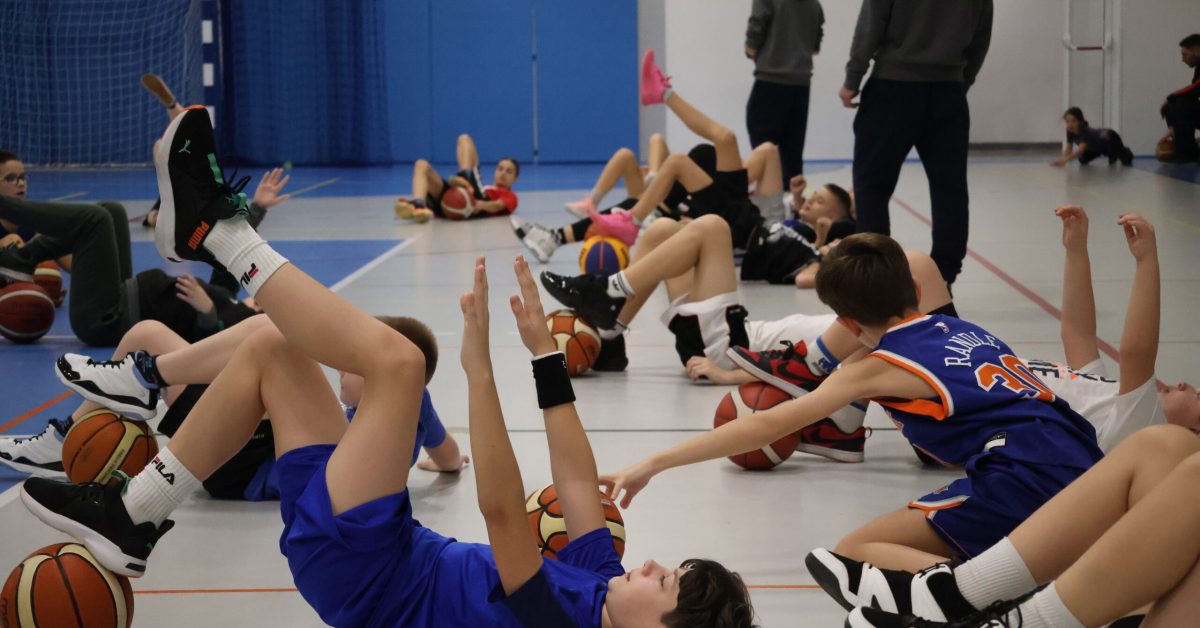 Grupa młodych koszykarzy leży na boisku, wykonując ćwiczenia.