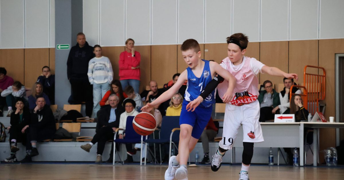 Dwóch młodych koszykarzy walczy o piłkę podczas meczu, jeden w niebieskiej koszulce, drugi w białej.