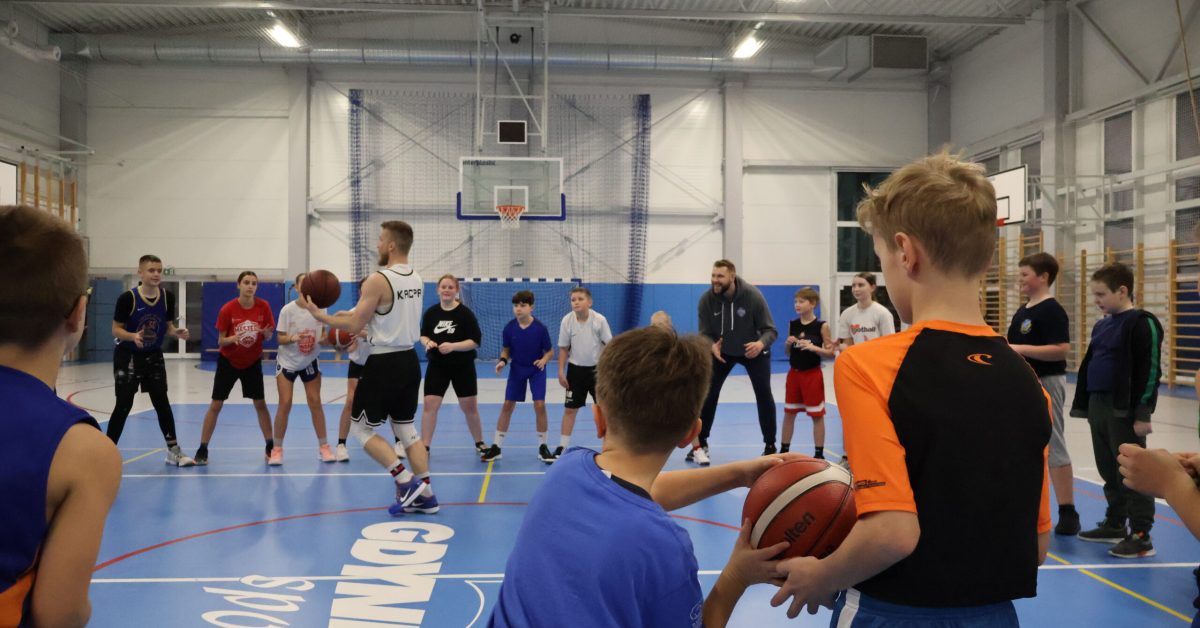 Dzieci w kółku na treningu koszykówki, w środku Kacpa