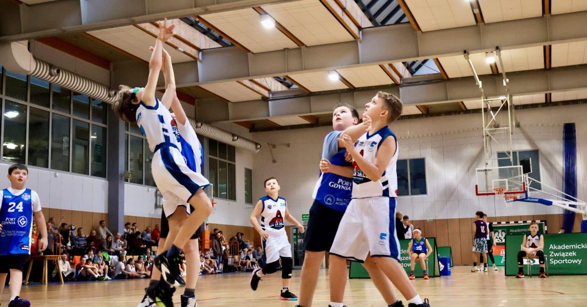 Ujęcie rzutu do kosza – chłopiec w białej koszulce wyskakuje, próbując zdobyć punkty.