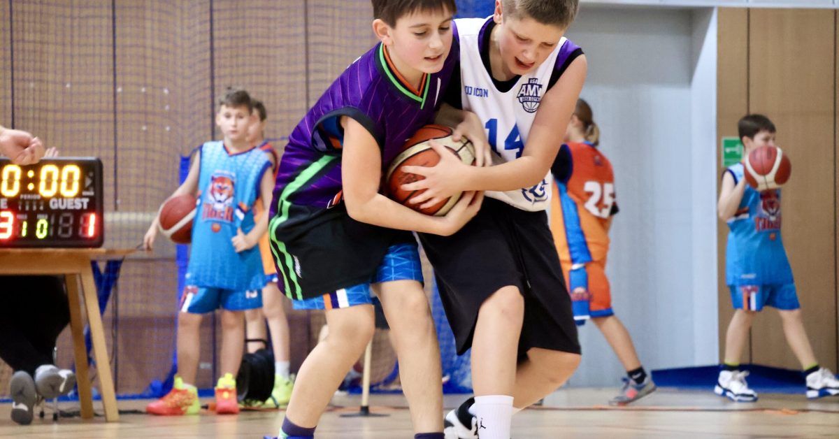 Dwóch chłopców energicznie walczy o piłkę, trzymając ją oburącz i próbując przejąć kontrolę.