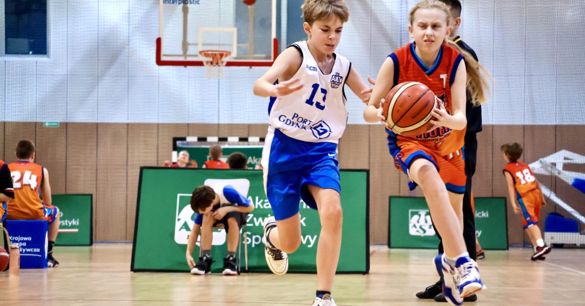 Chłopiec w białej koszulce i dziewczynka w czerwonej koszulce rywalizują o piłkę podczas meczu.