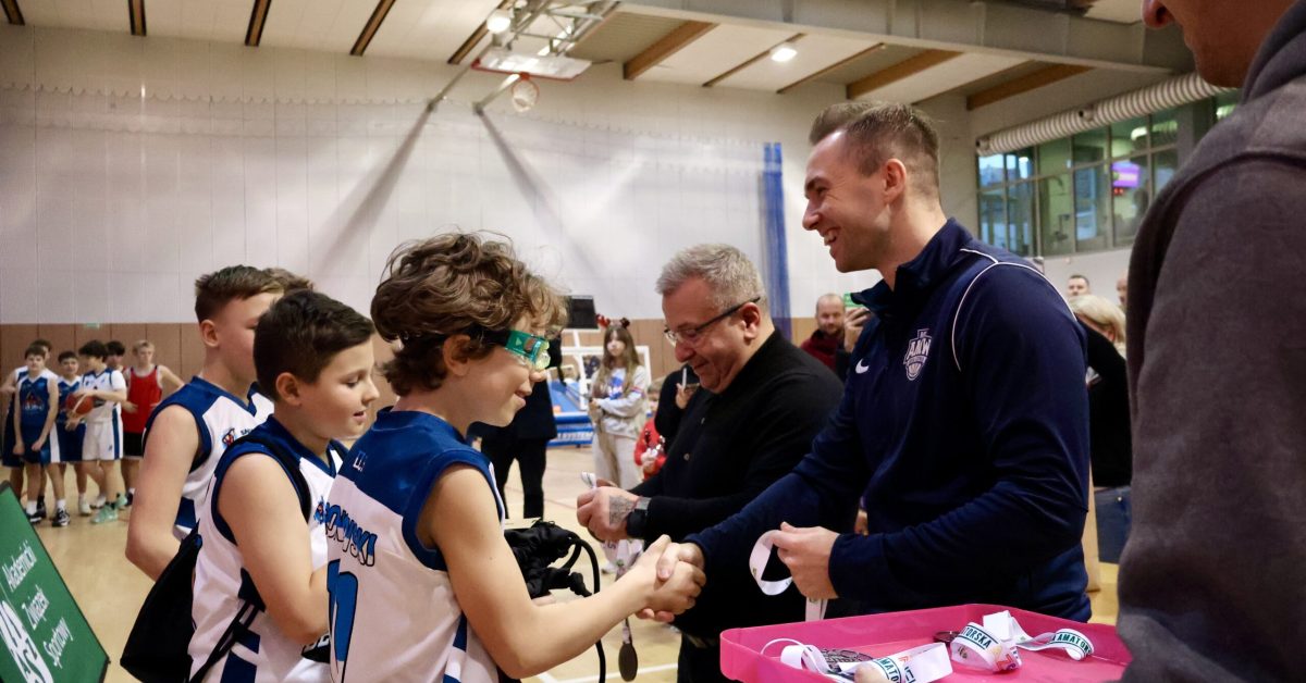 Trener ściska dłonie młodych zawodników w koszulkach sportowych po zakończonym meczu.