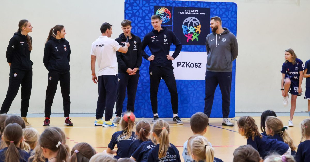 Zawodniczki i zawodnicy w czarnych strojach stoją przed grupą dzieci, prowadząc zajęcia sportowe dla przedszkolaków.