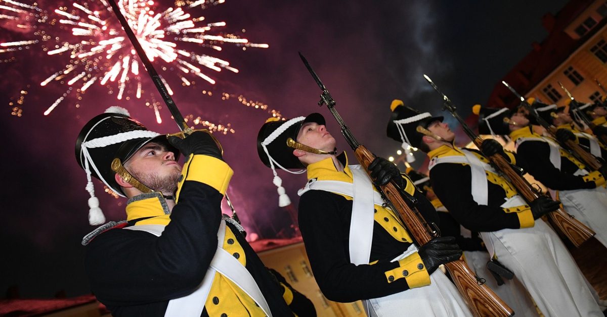 Grupa marynarzy w mundurach w trakcie pokazu z fajerwerkami na nocnym niebie.