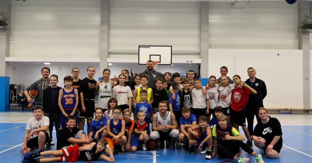 Zdjęcie grupowe uczestników treningu koszykarskiego na hali sportowej.